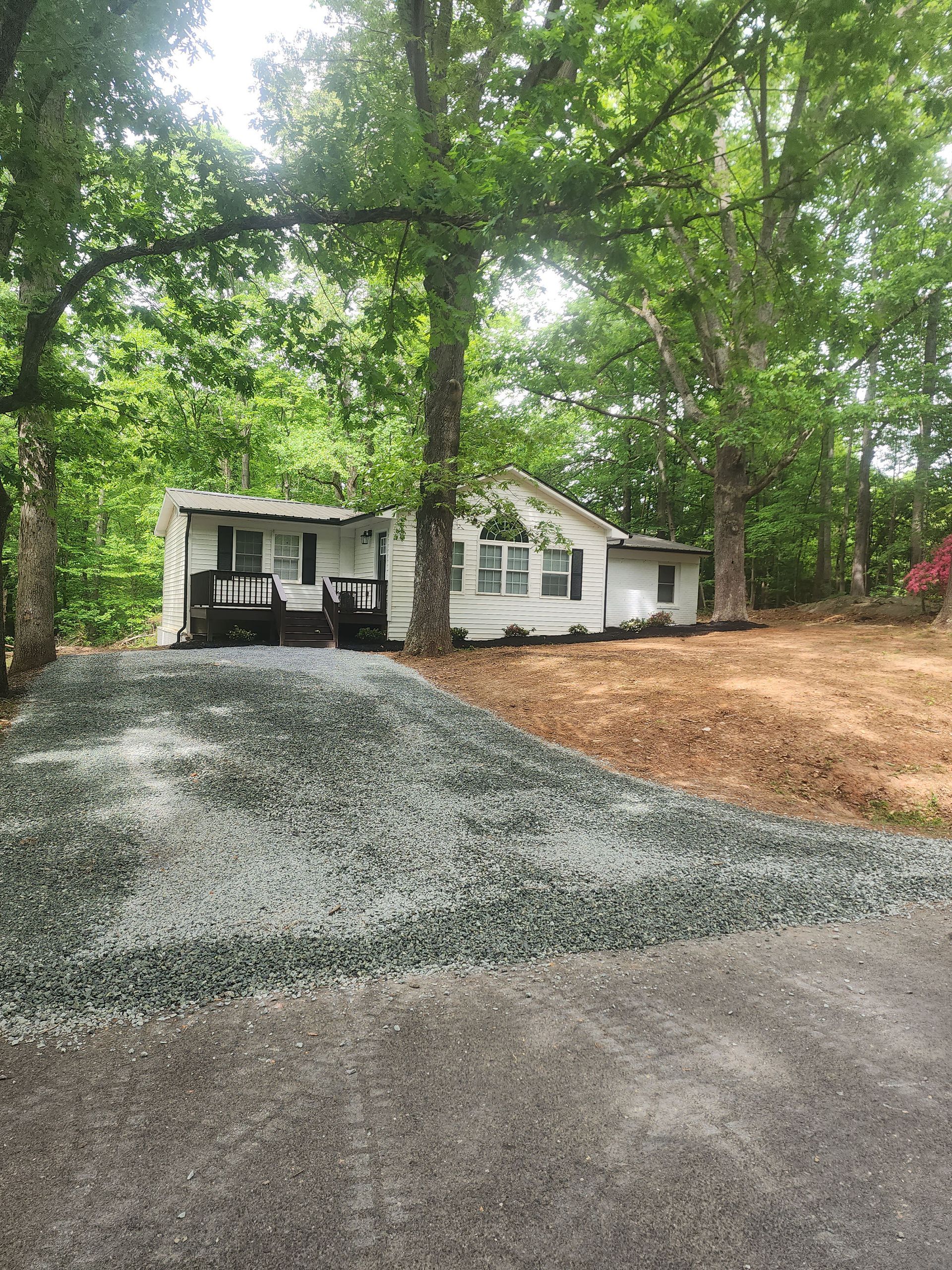A white house is sitting on top of a hill next to a gravel driveway.