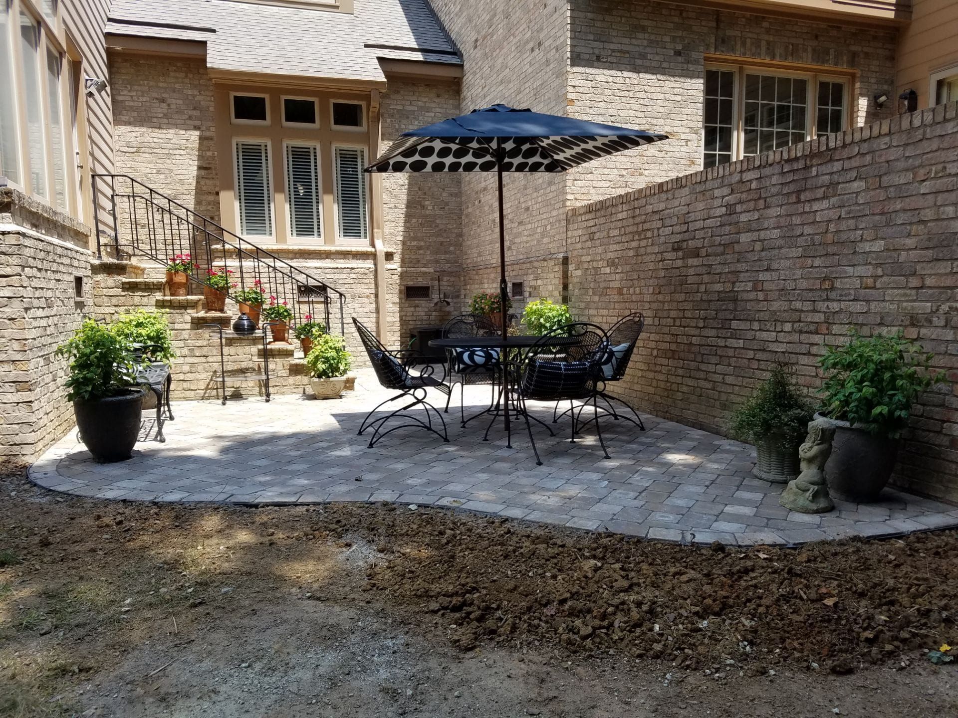 A patio with a table and chairs and an umbrella in front of a brick building.