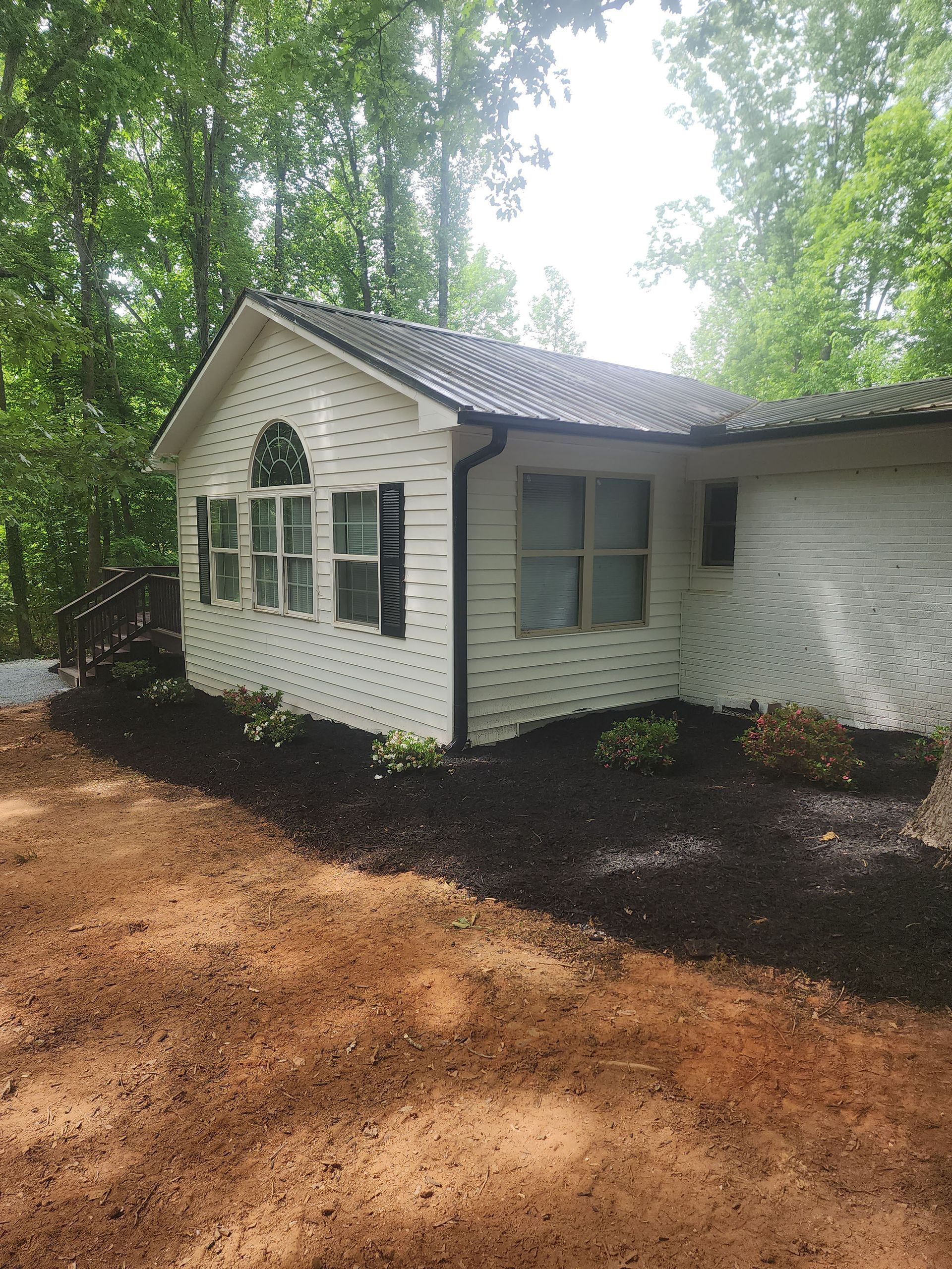 A white house with a black roof is surrounded by trees.