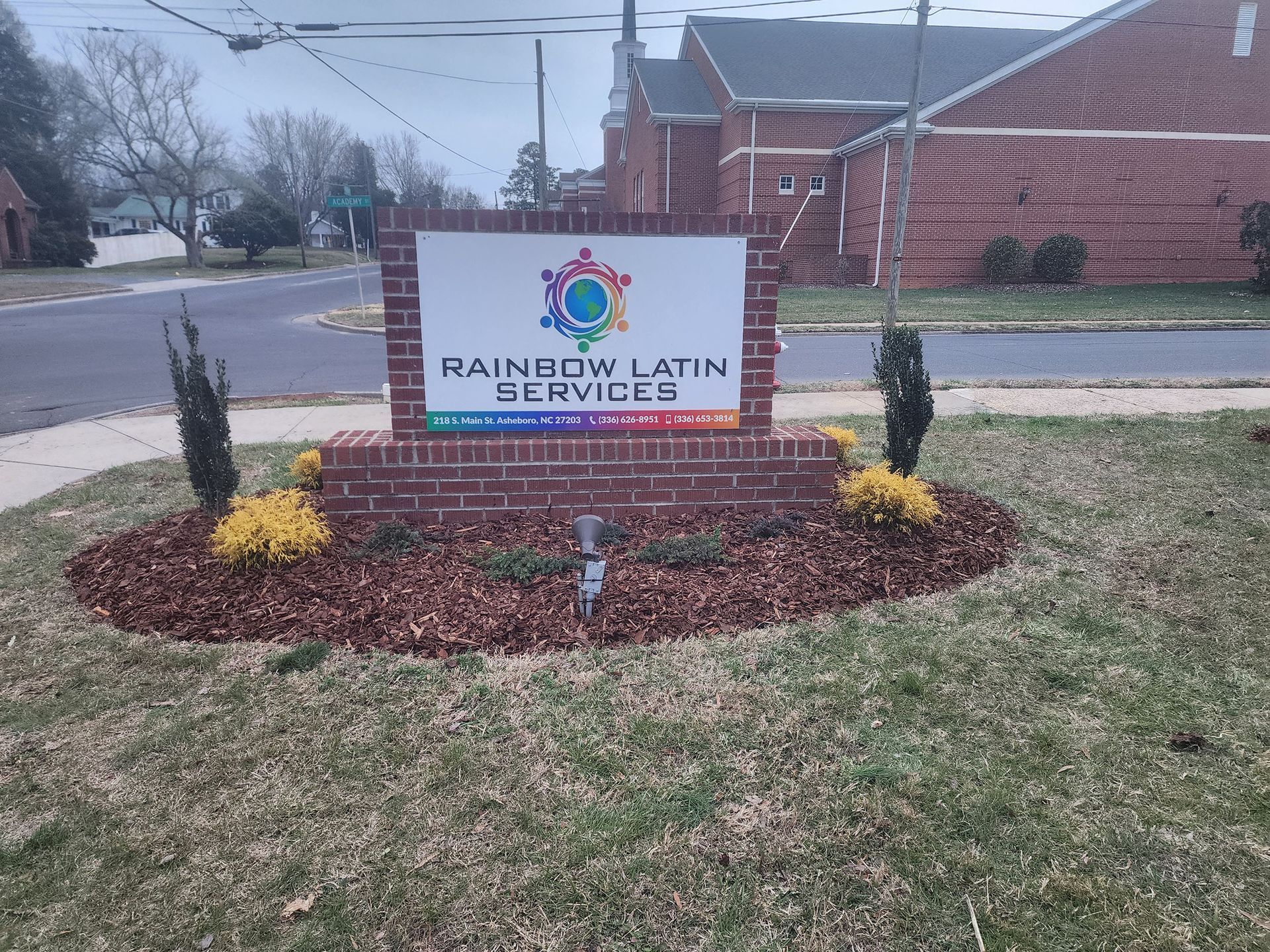 A sign for rainbow latin services is sitting in the middle of a lush green field.