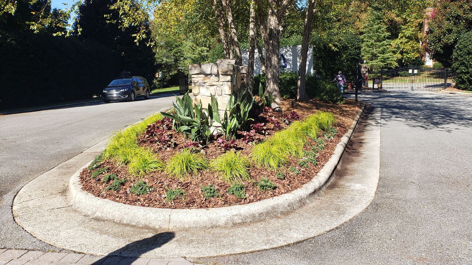 A circular garden in the middle of a road with trees in the background.