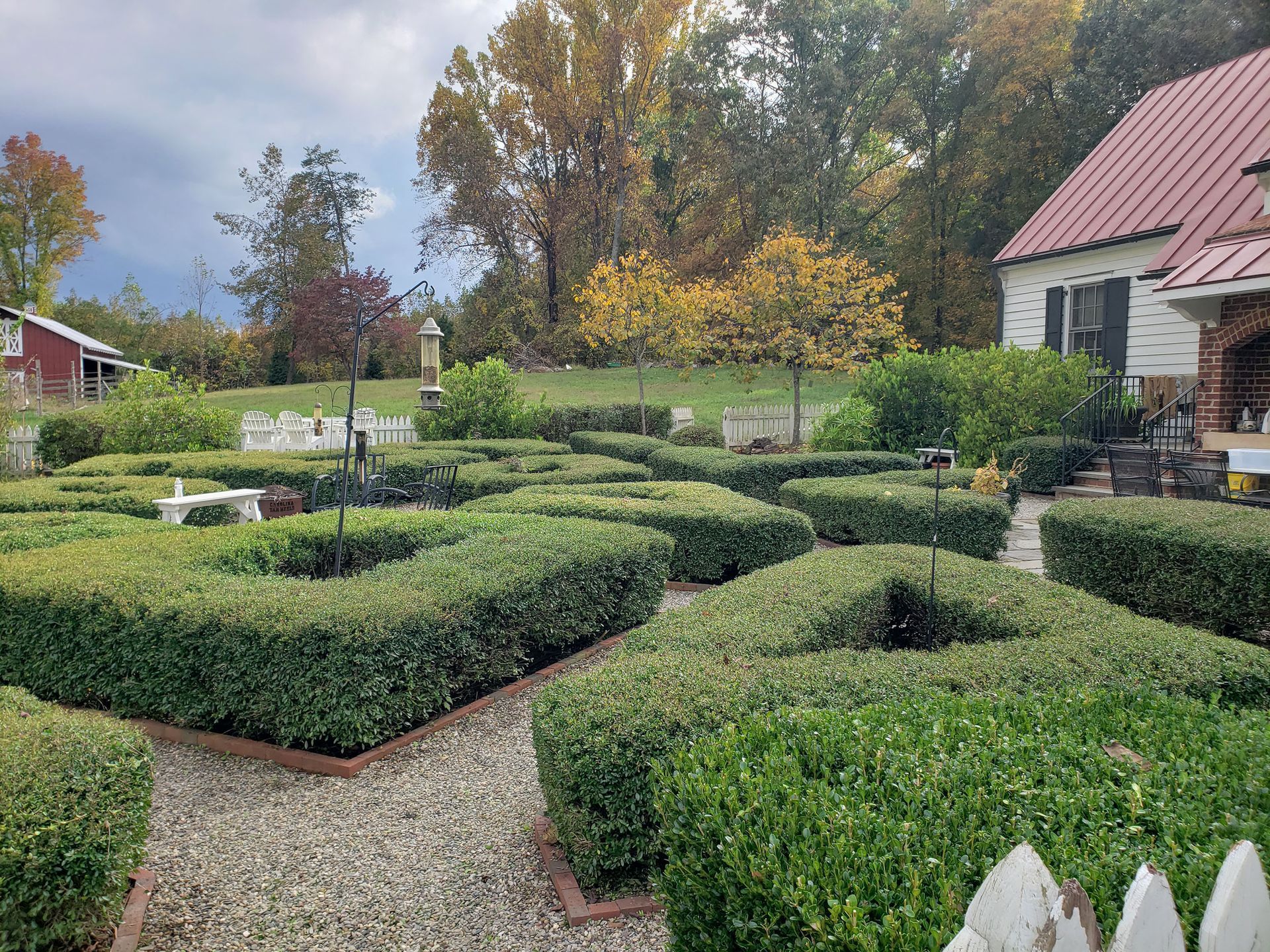 There is a maze in the middle of the garden with a house in the background.