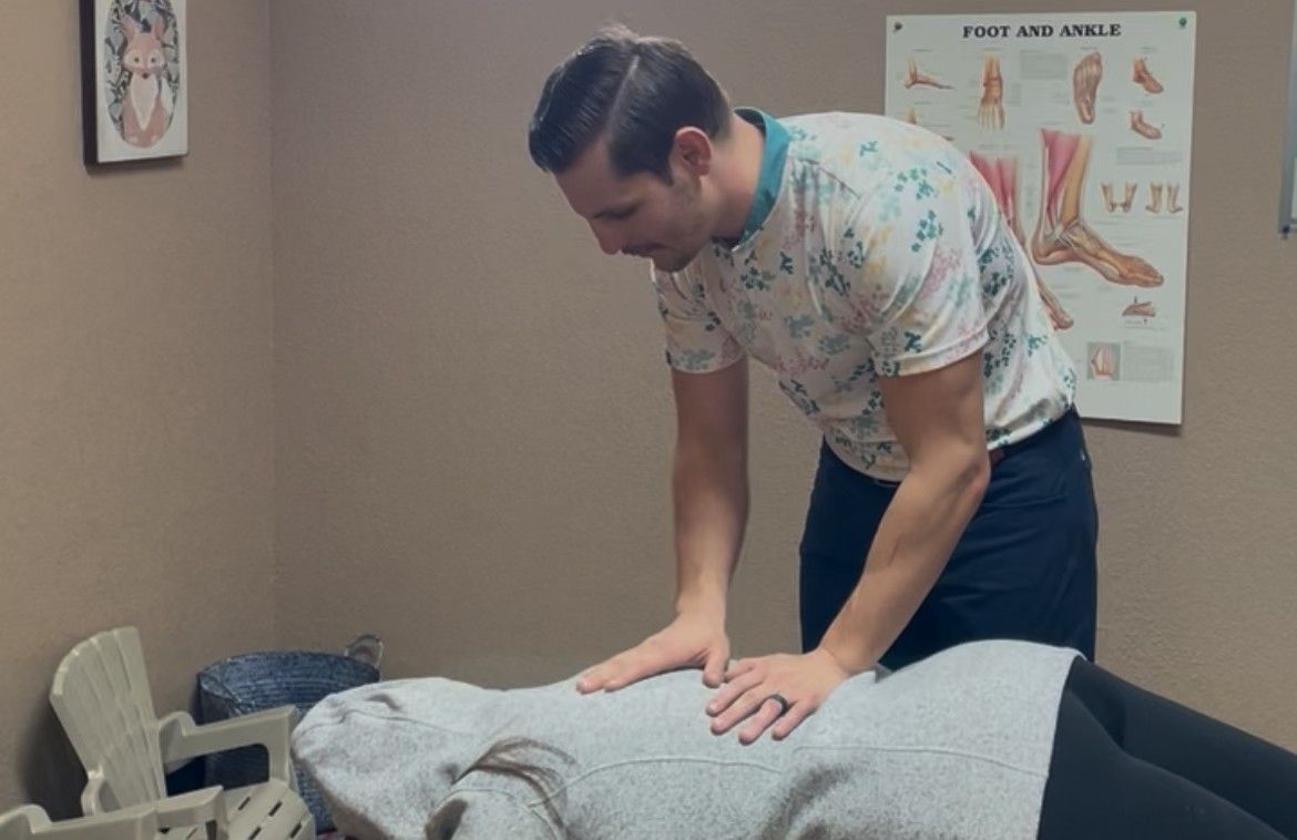A man performing a massage on a person lying on a table in a treatment room.