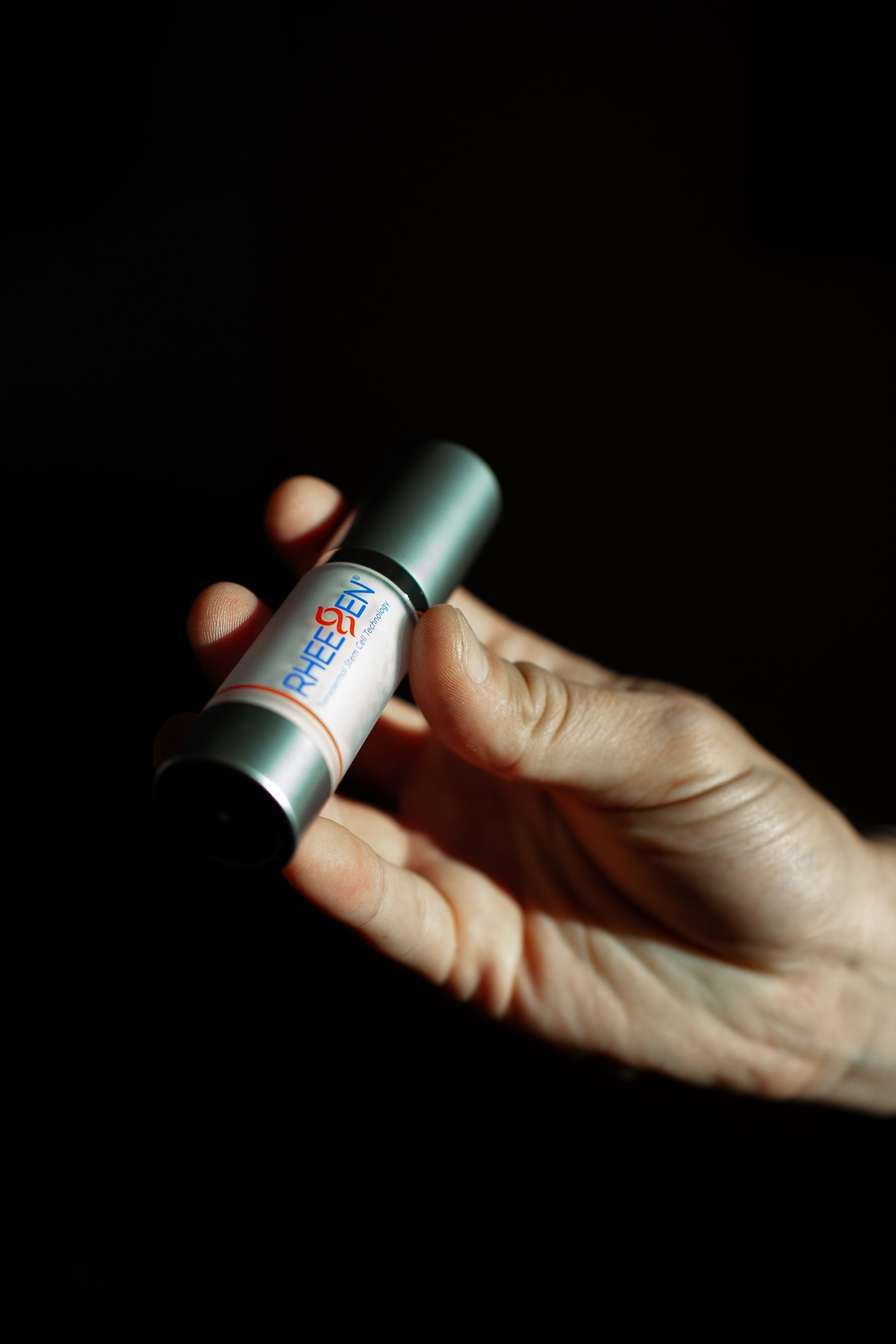 Hand holding a silver roll-on bottle with a white label and blue and red accents.
