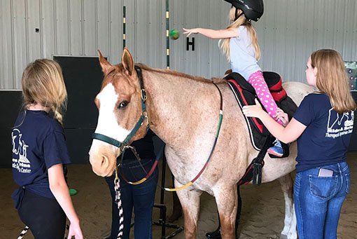 A little girl is riding on the back of a horse.