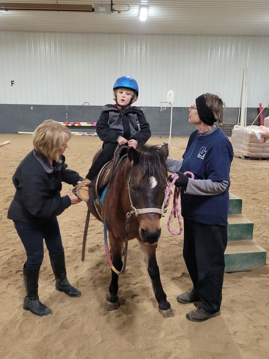 A little boy is riding a pony in an indoor arena