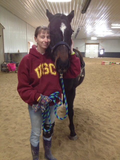 A woman wearing a usc sweatshirt stands next to a horse