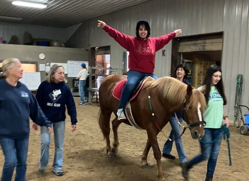 A group of people are working on a horse in a barn.