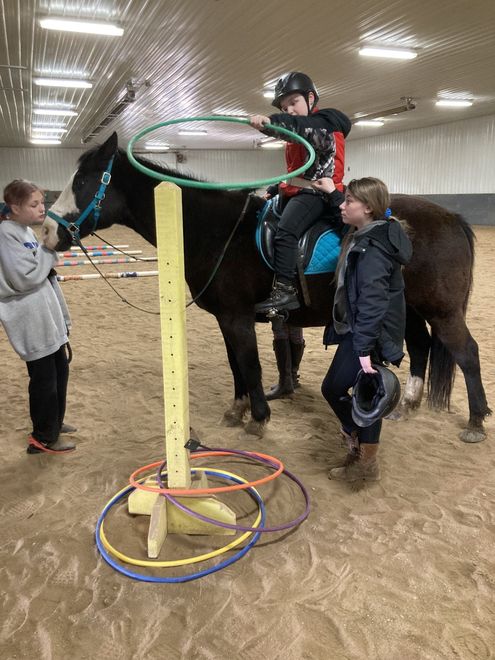 A young boy is riding a horse in an indoor arena while playing with hula hoops.