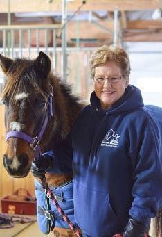 A woman is standing next to a brown horse in a stable.