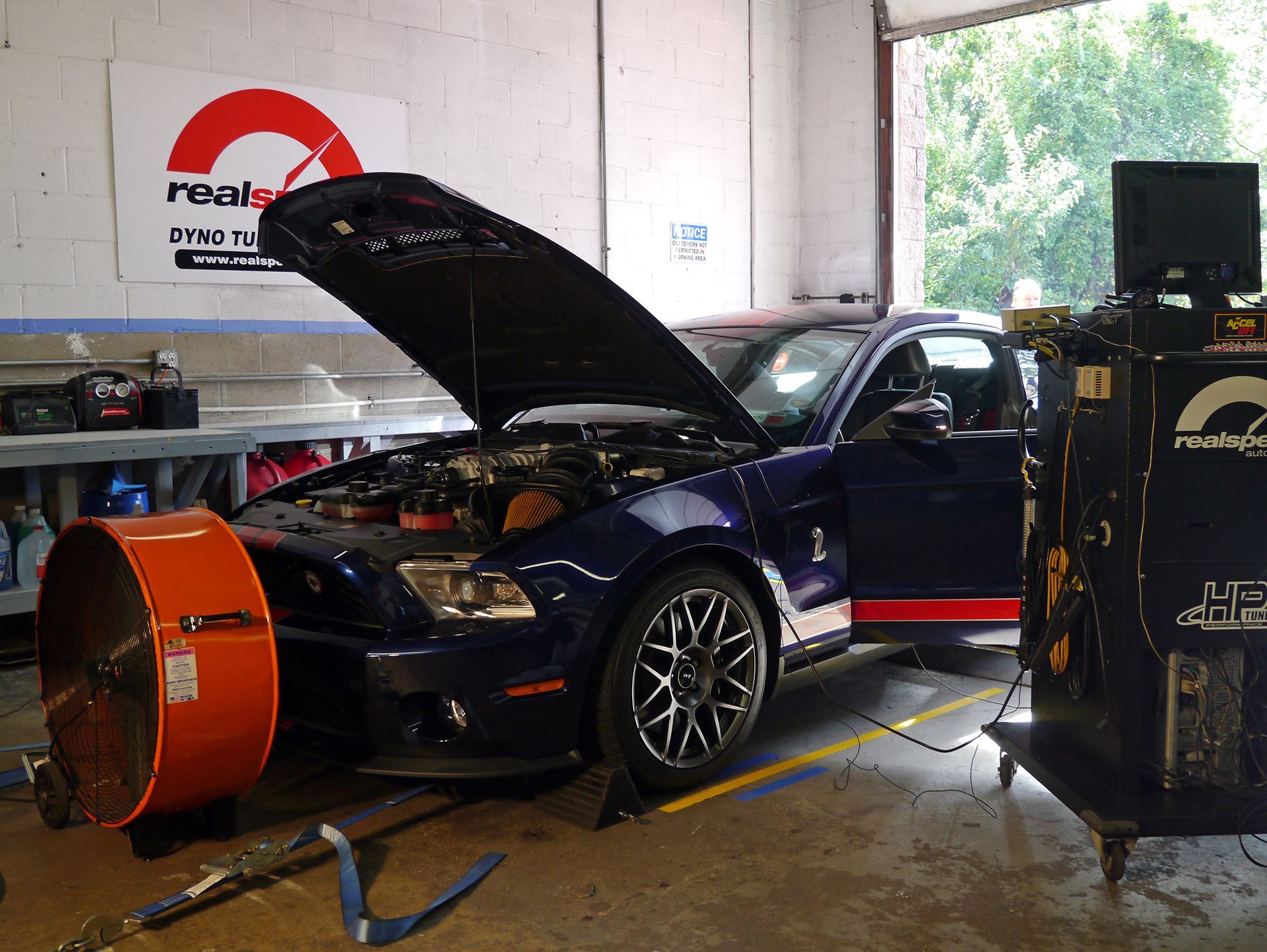 A blue ford mustang with the hood up in a garage