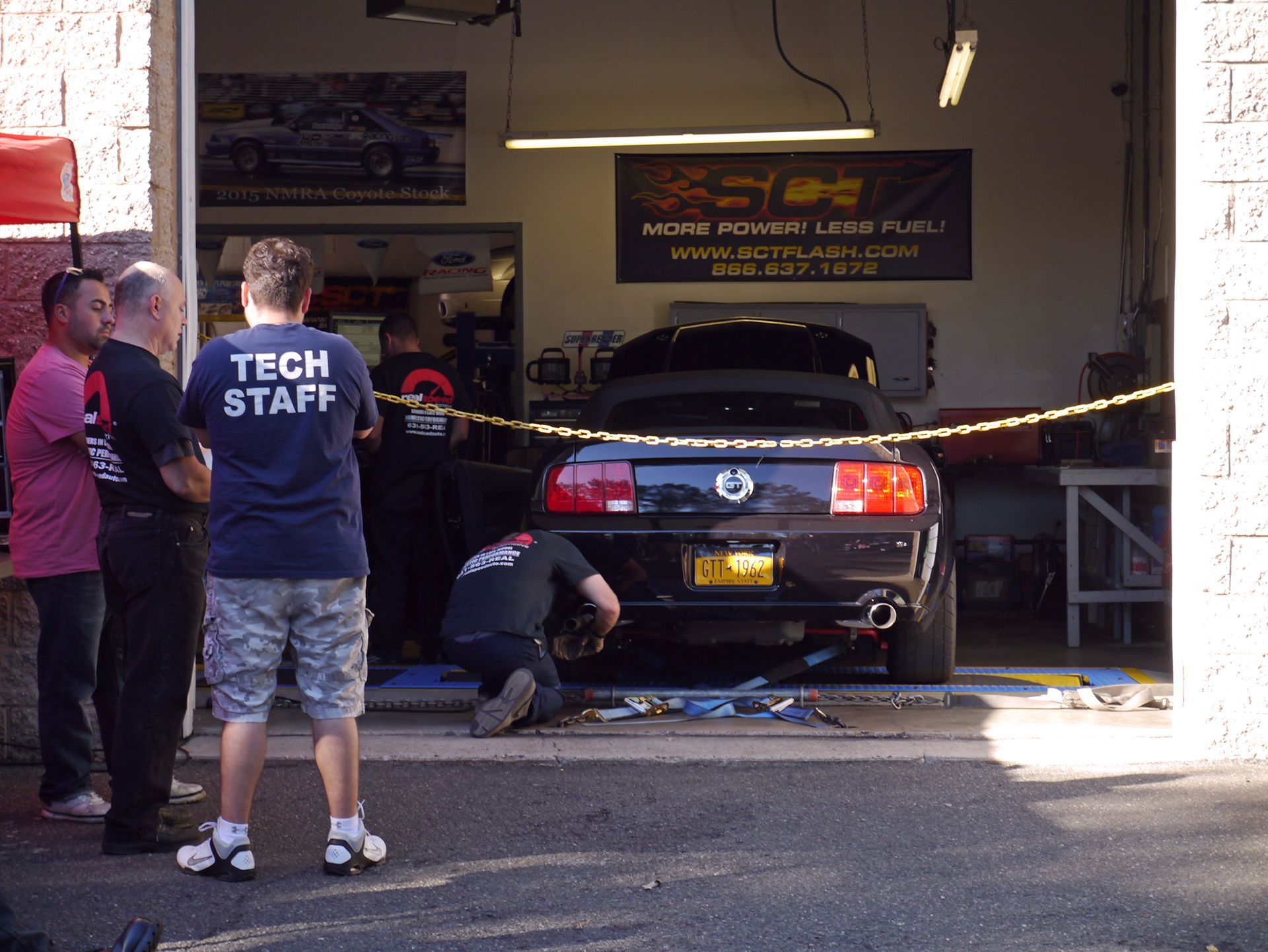 A man in a tech staff shirt stands in front of a car