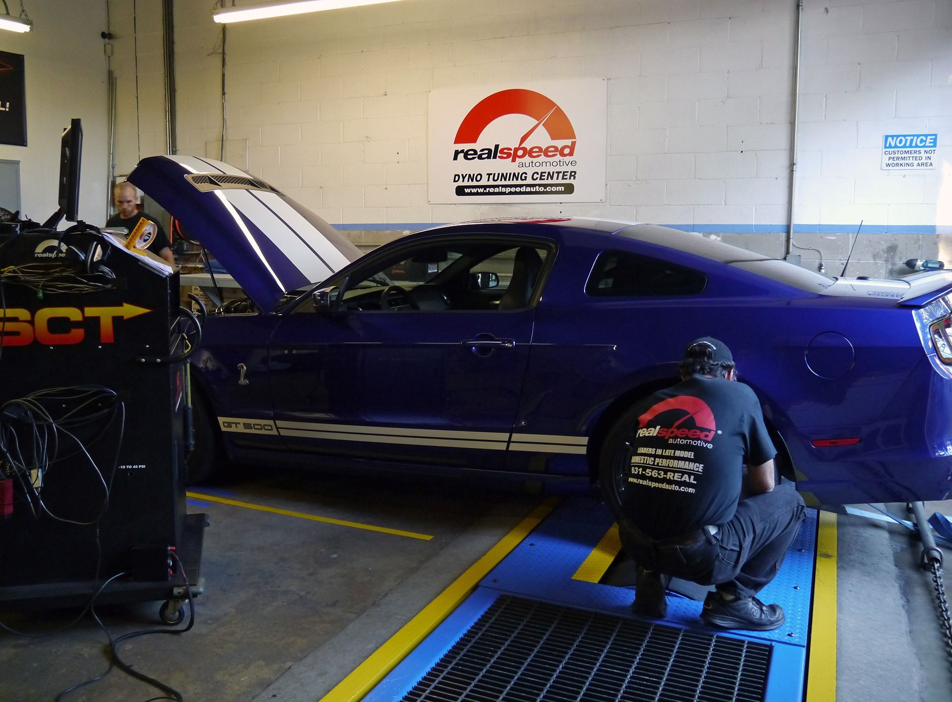 Two men are working on a blue mustang in a garage