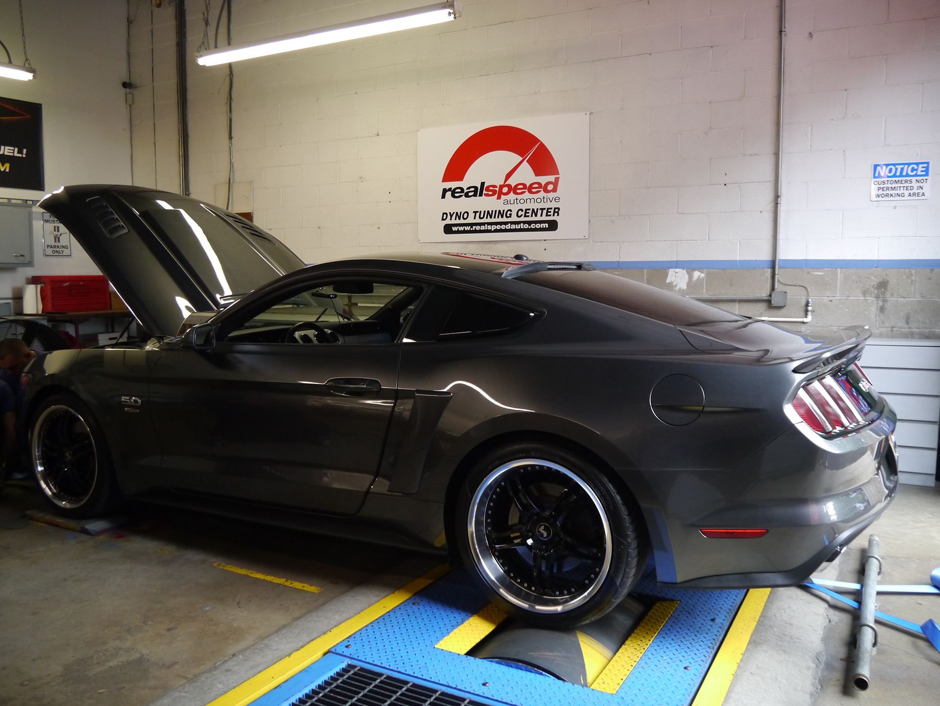 A mustang is being tested in a garage with the hood up
