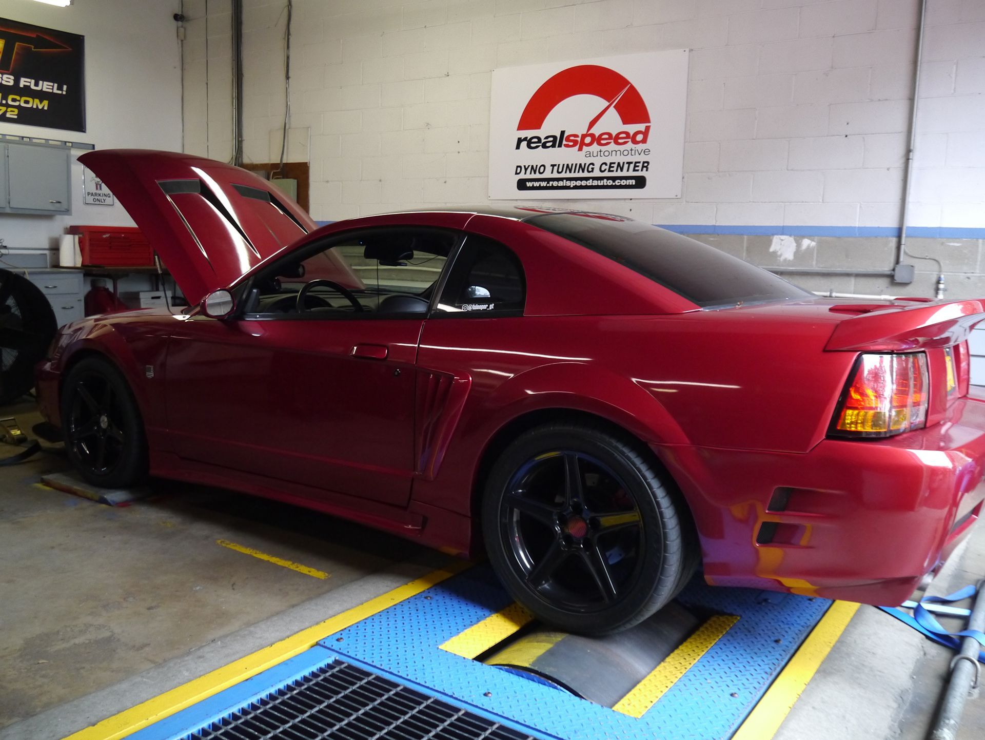 A red mustang is sitting on a dyno with the hood up