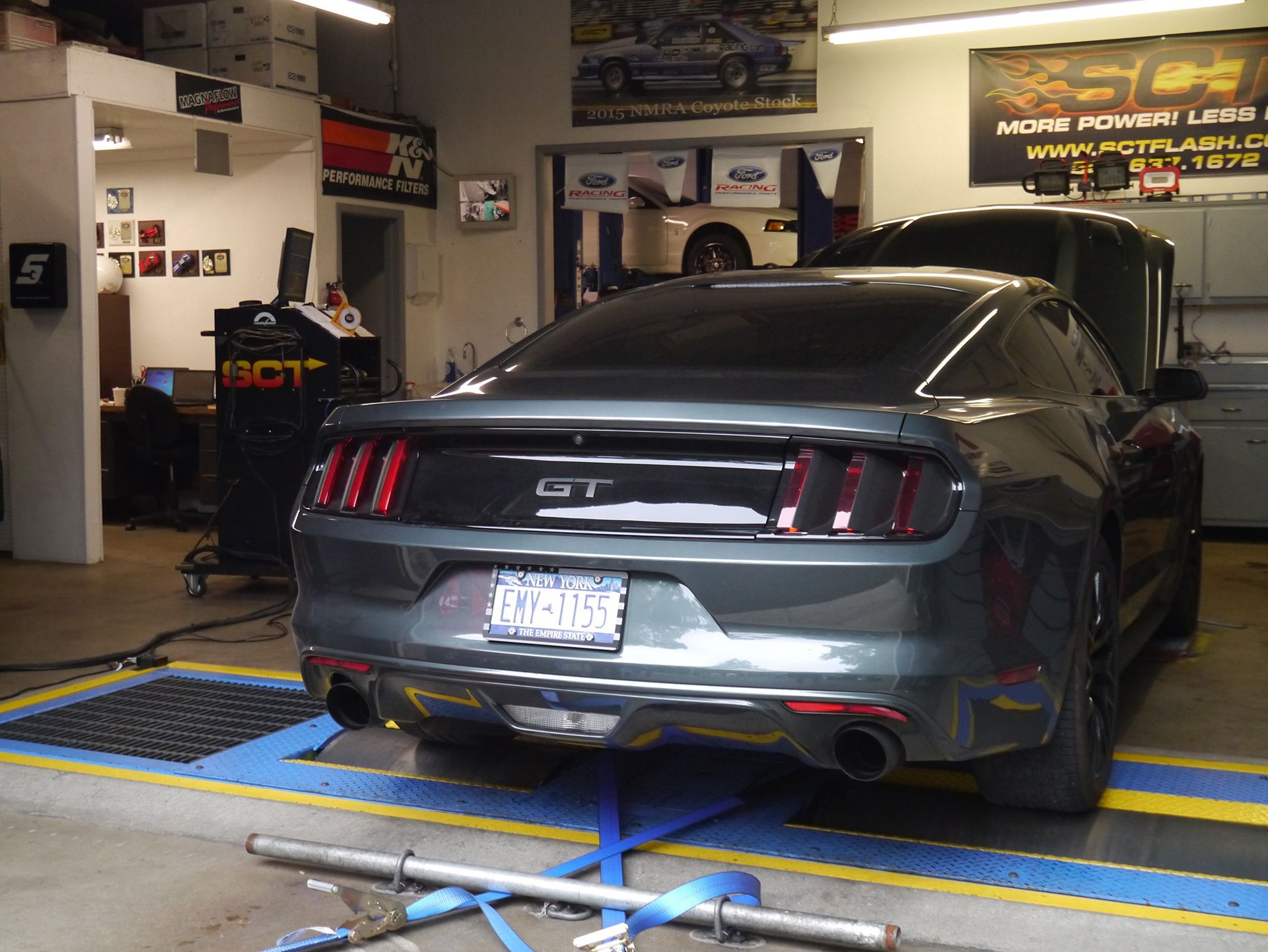 A gray mustang is parked in a garage with the hood open