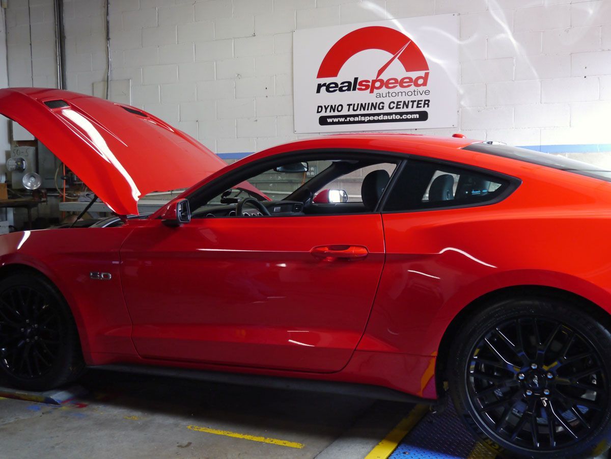 A red car with the hood up is in front of a real speed sign