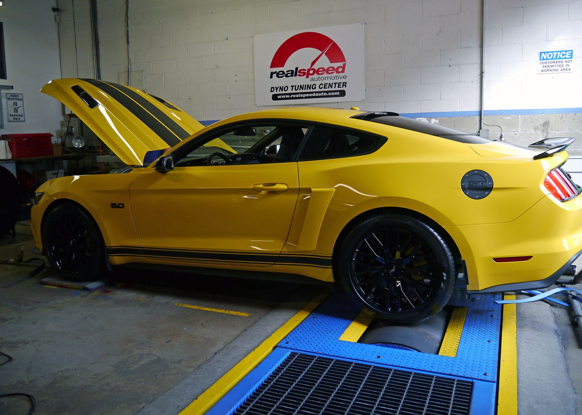 A yellow mustang is sitting on a dyno in a garage