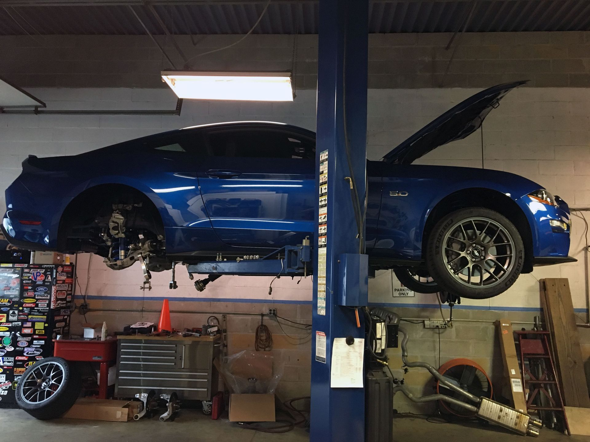 Blue Ford Mustang on a car lift with the hood open, inside a garage.