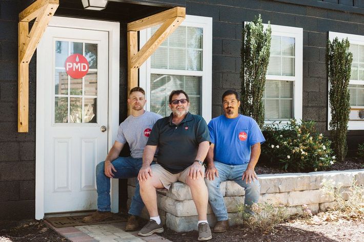 Three men are sitting on a stone wall in front of a building.
