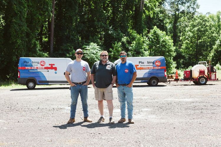 Three men are standing in a parking lot in front of two vans.
