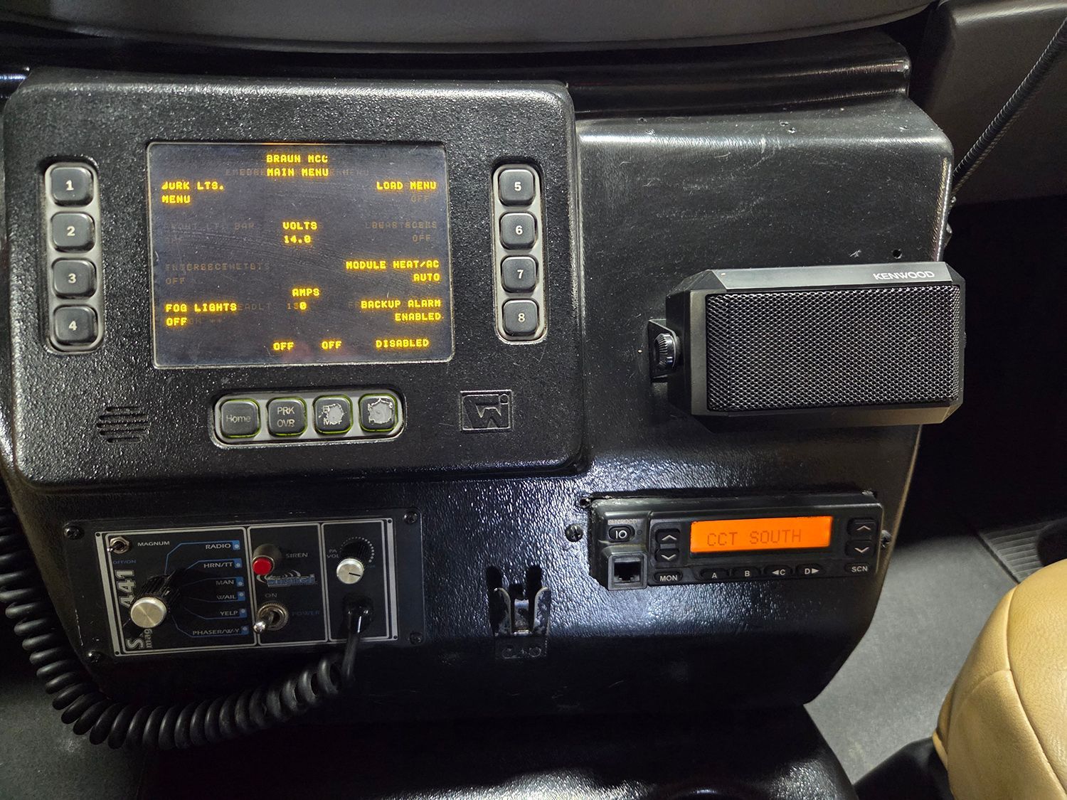 Vehicle dashboard control panel with a lit display, buttons, and a radio unit on a dark interior console