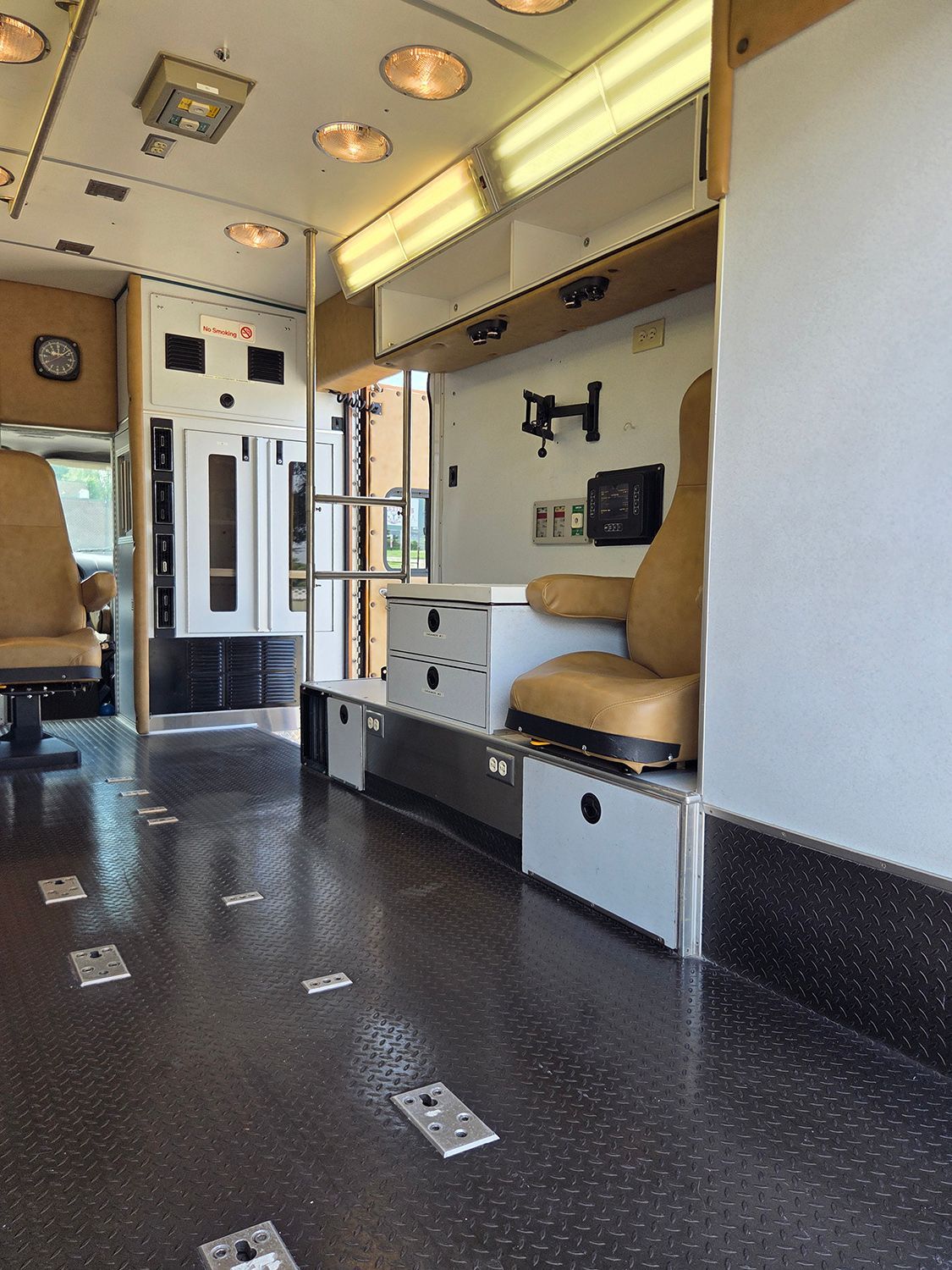 Interior of an ambulance with beige seats, grab bars, and a dark speckled floor.