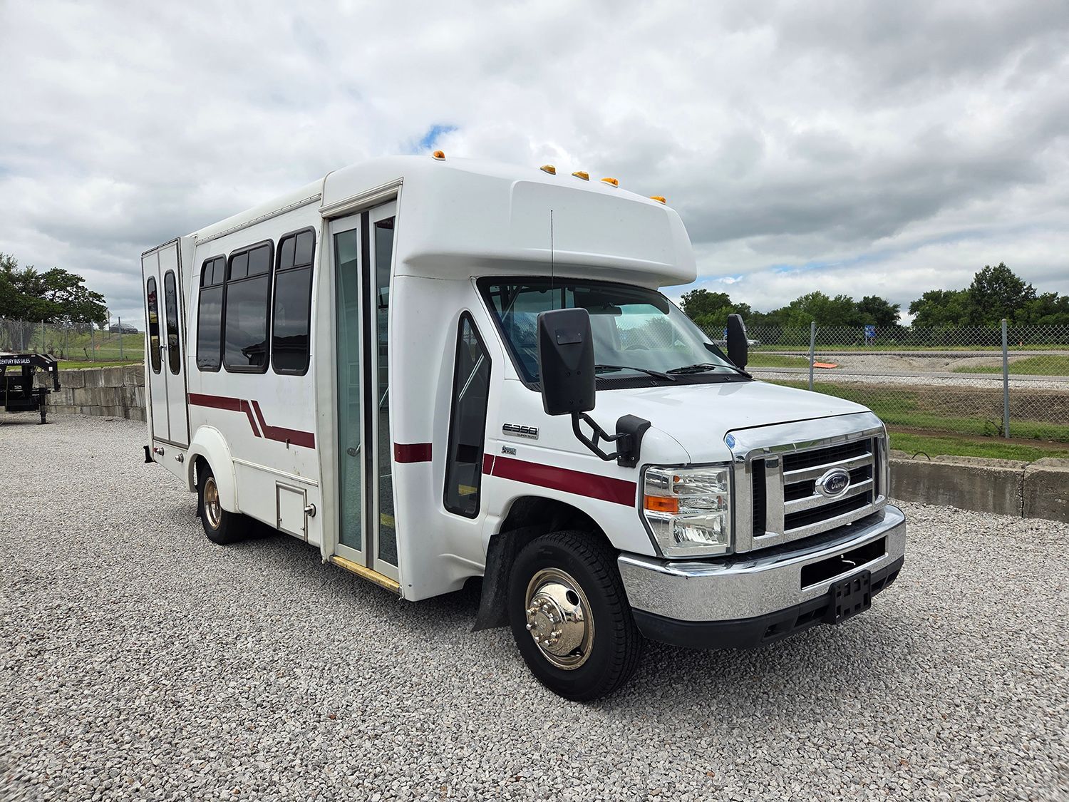 White shuttle bus parked on gravel under cloudy sky