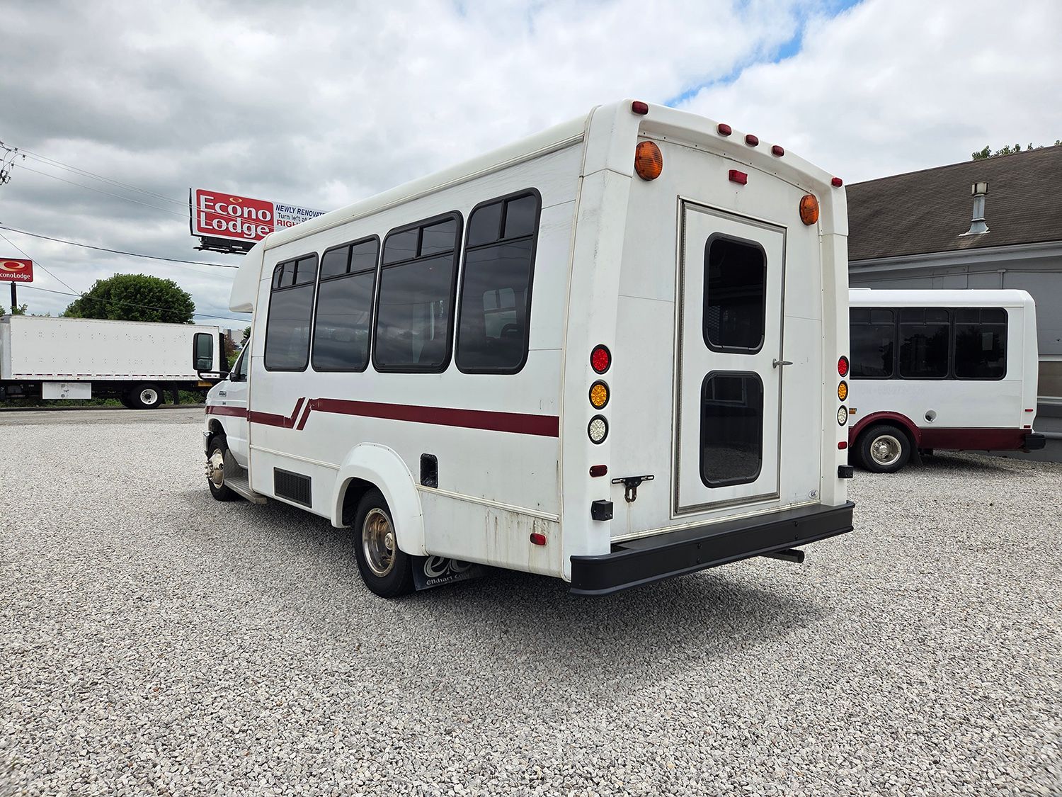 White shuttle bus with tinted windows parked on a gravel lot under a cloudy sky