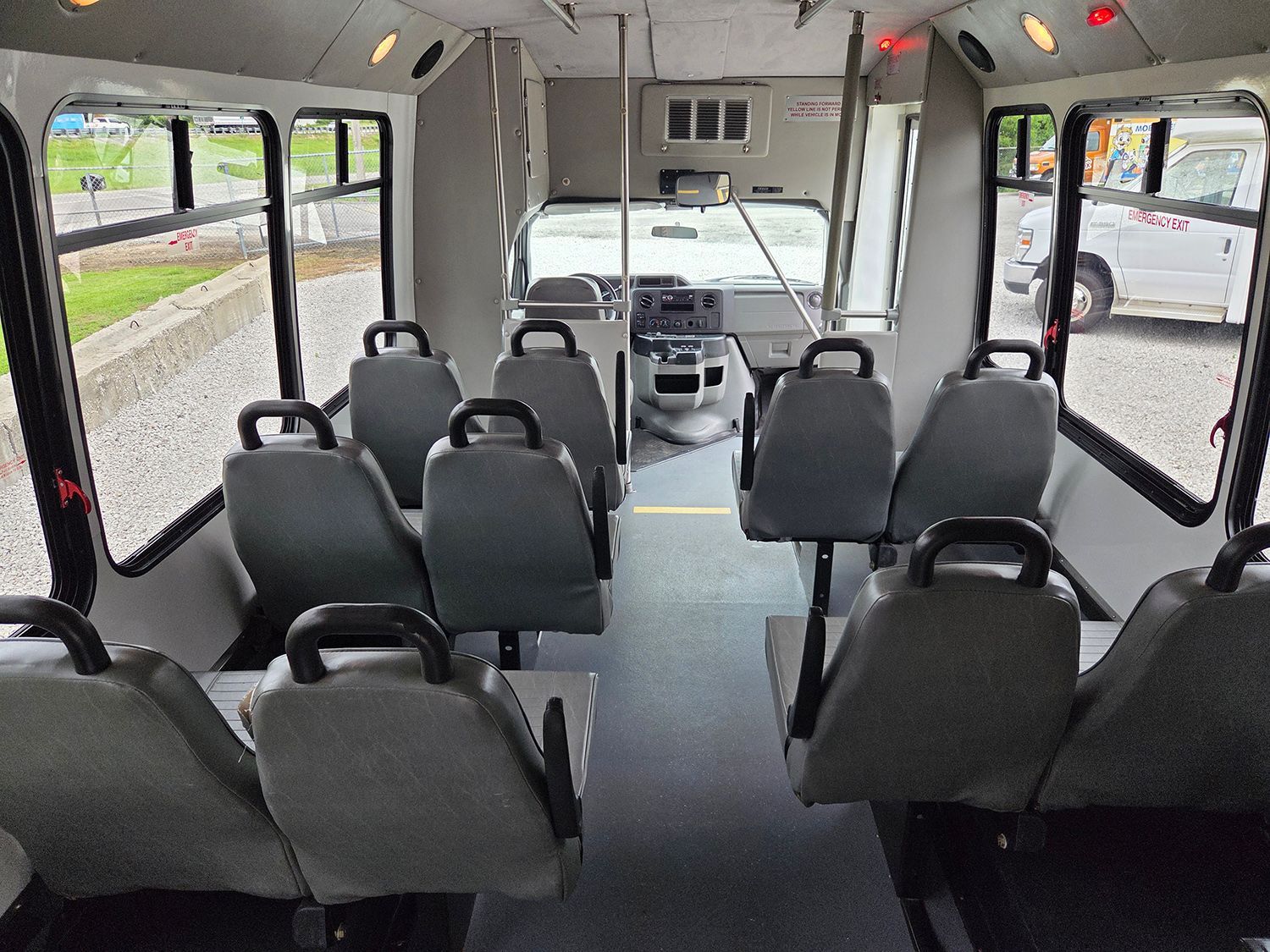 Empty shuttle bus interior with rows of gray seats and large windows.
