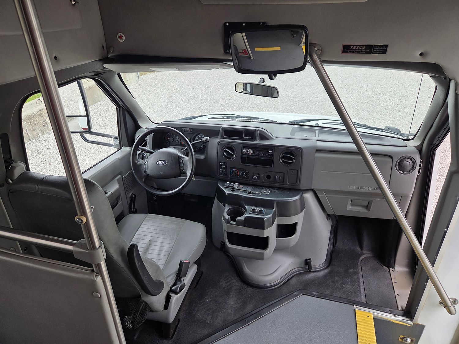 Vehicle interior with steering wheel, dashboard, seats, and metal support bars in the cabin.