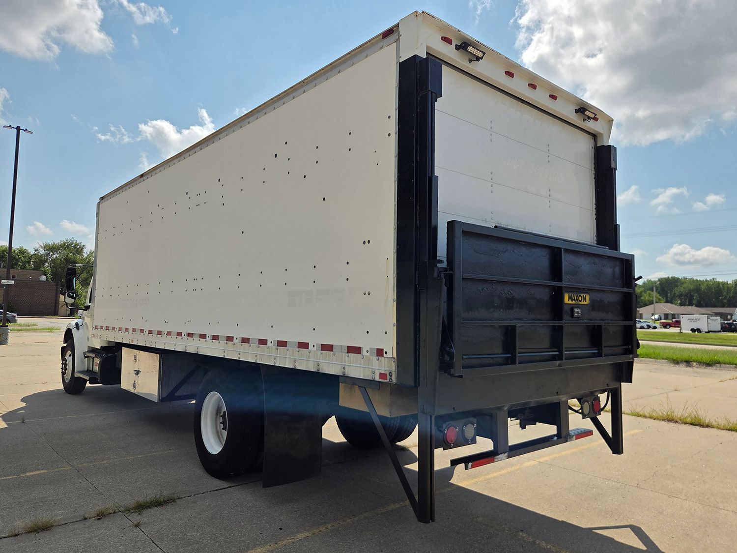 White box truck with black rear liftgate parked outdoors under a blue sky