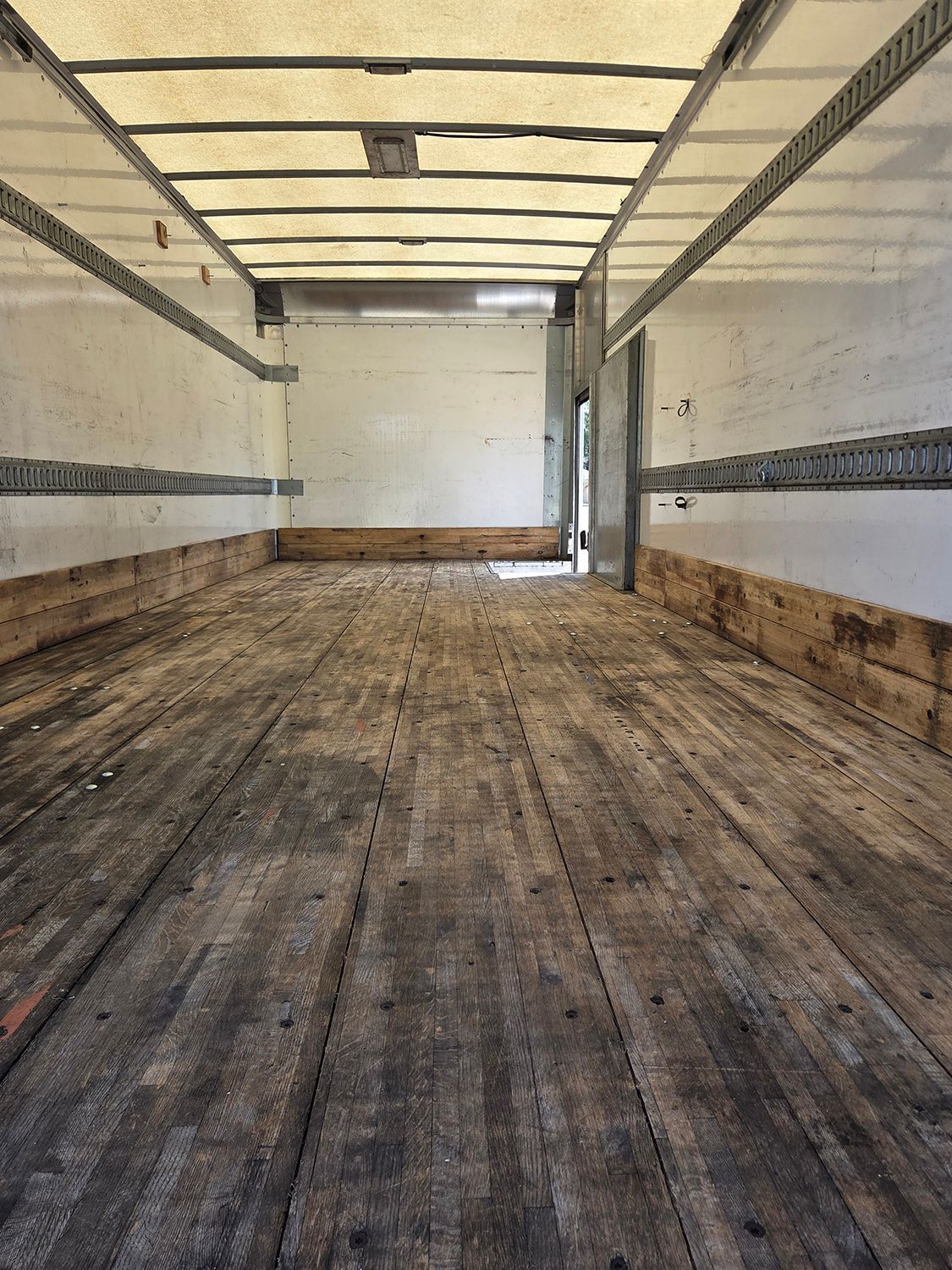 Empty box truck interior with wooden floor and white walls, viewed from the rear to the front loading area