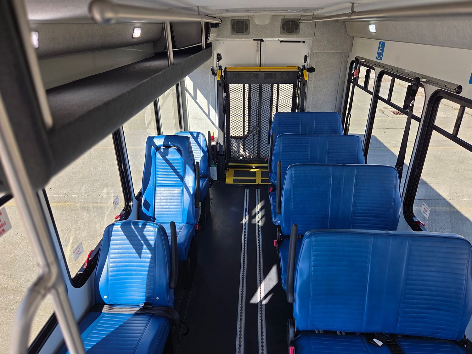 Empty bus interior with blue seats and black railings, viewed from the rear toward the front.
