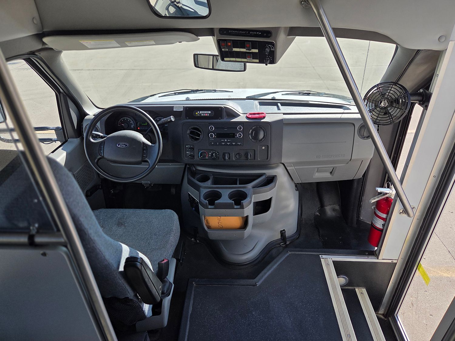 Interior of a bus or shuttle, showing the driver’s seat, dashboard, and front cabin area