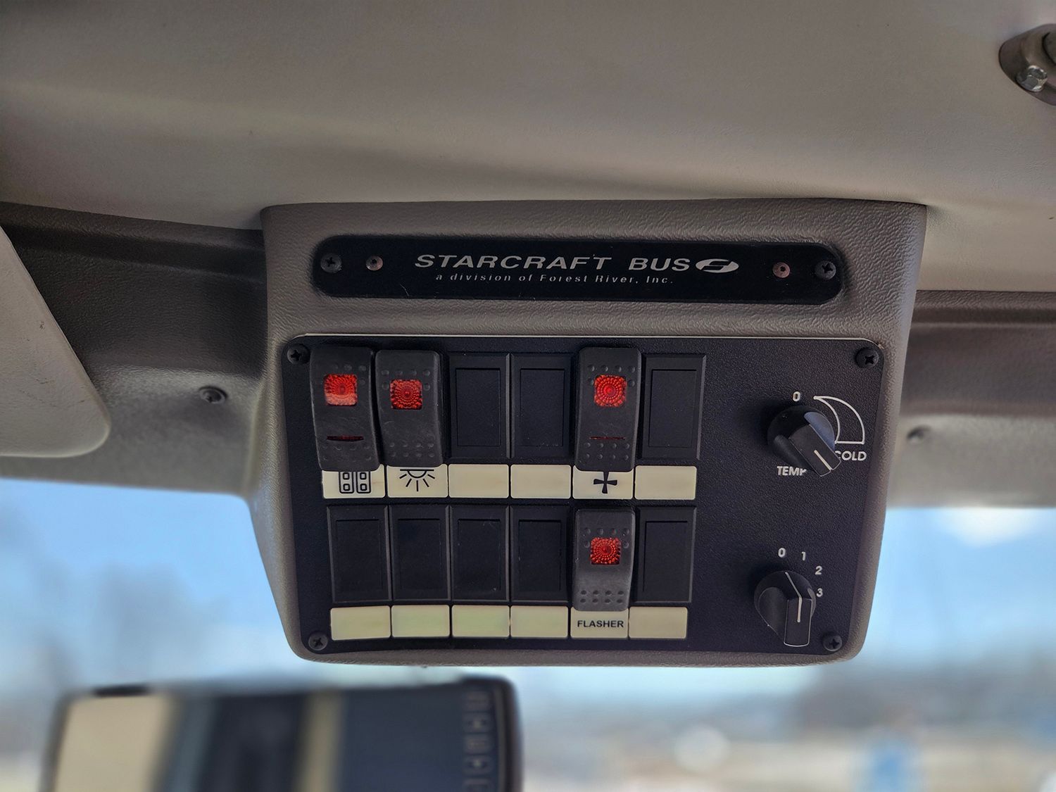 Overhead car control panel with black switches, red indicators, and two knobs mounted near the windshield