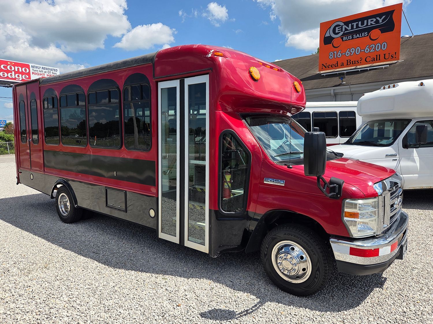 Red bus with black windows parked on a gravel lot near a dealership sign