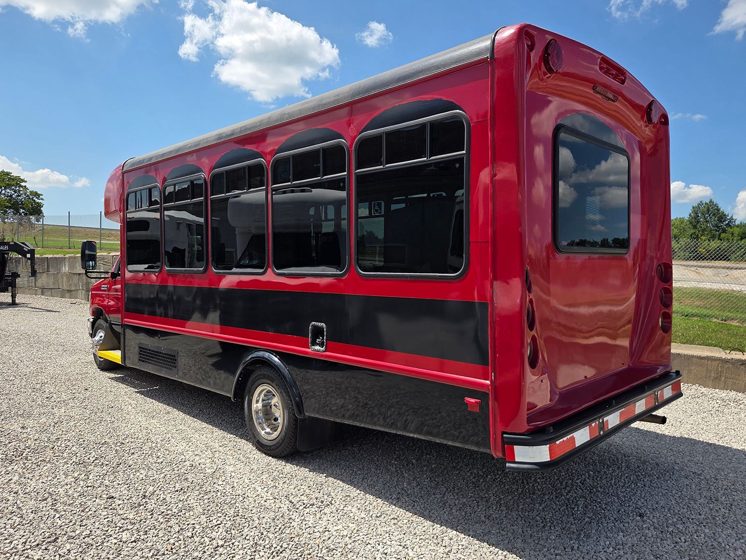 Red shuttle bus with black windows parked on gravel under a blue sky