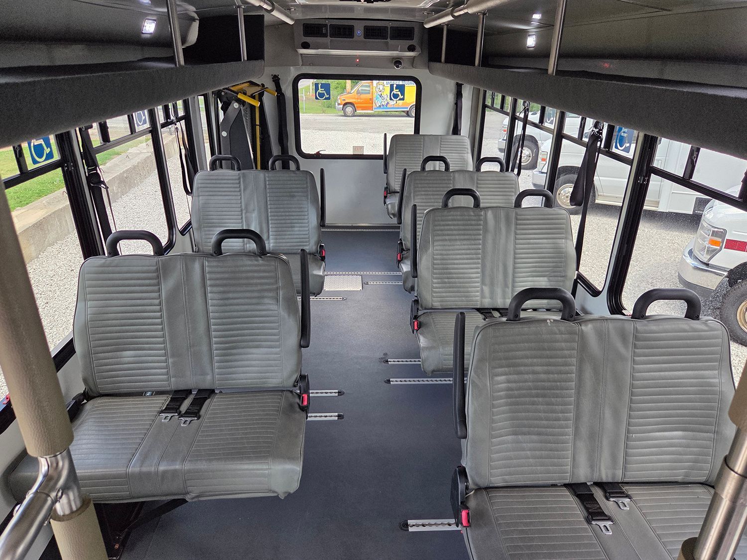 Empty bus interior with gray seats and large windows, viewed from the front toward the back.