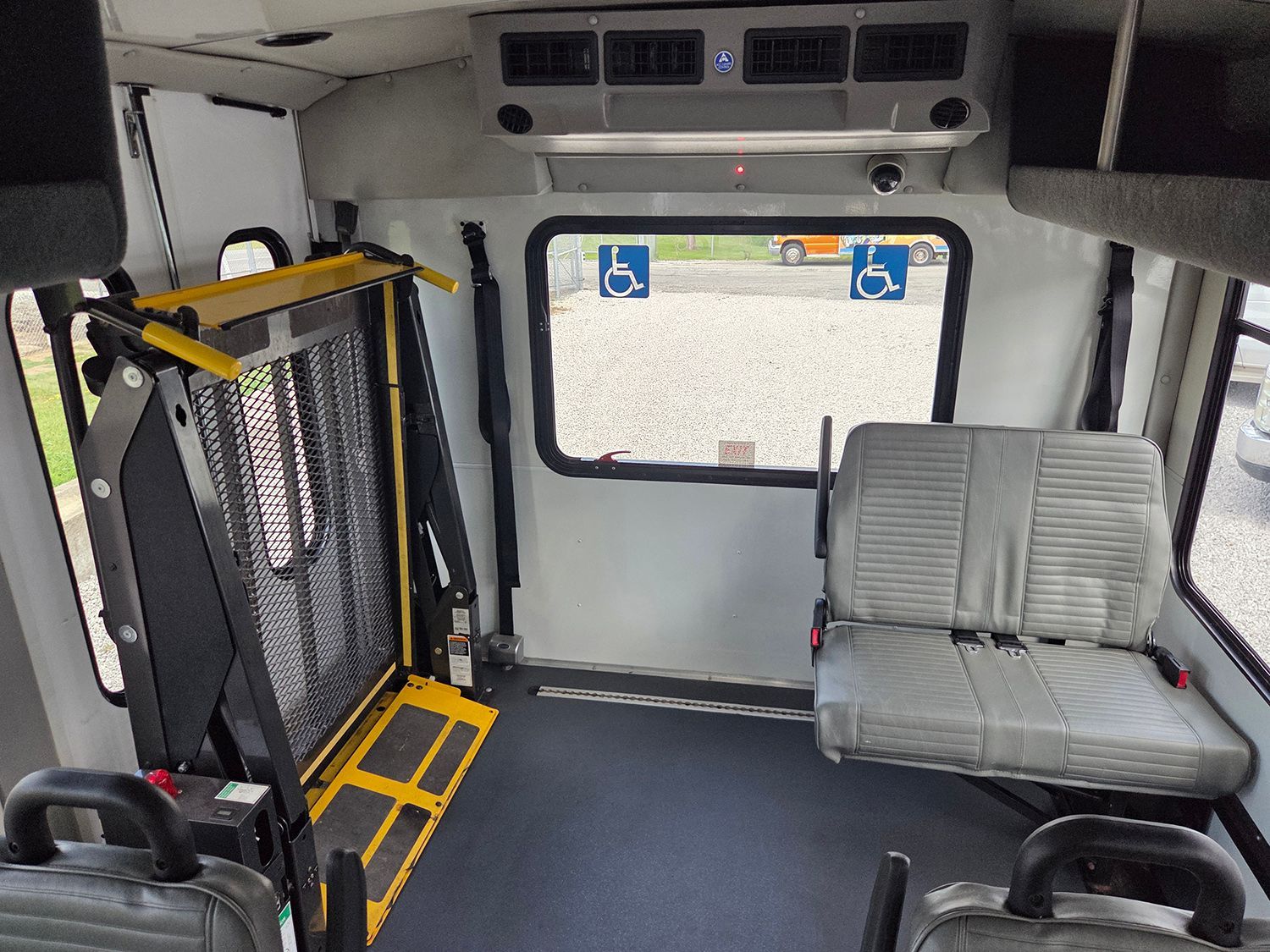 Accessible bus interior with a wheelchair lift, gray seat, and large side window.