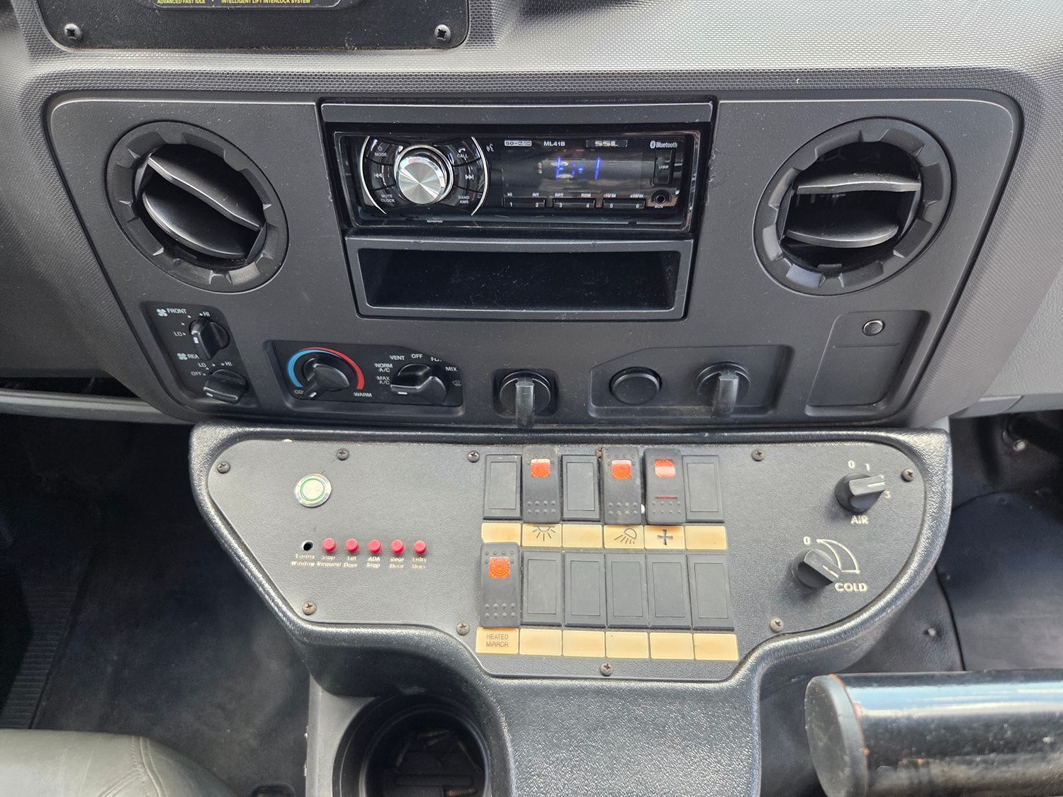 Vehicle dashboard with radio, vents, and a custom control panel with illuminated switches and knobs