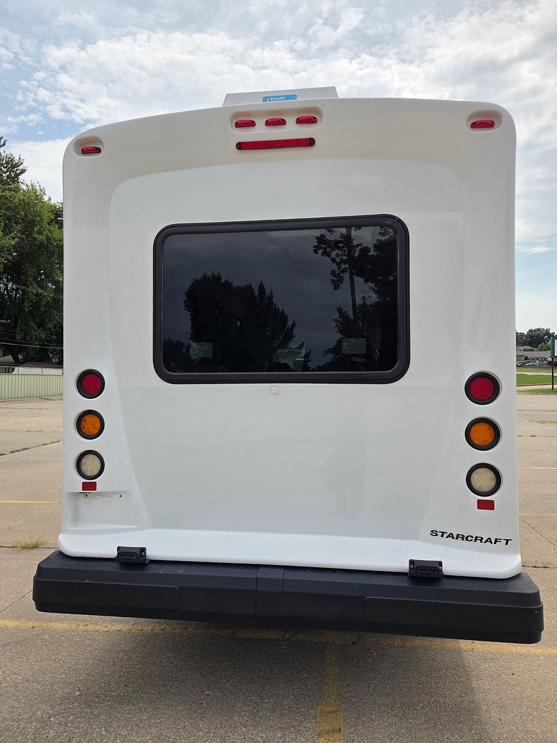 Rear view of a white shuttle bus with tinted window and red lights parked outdoors