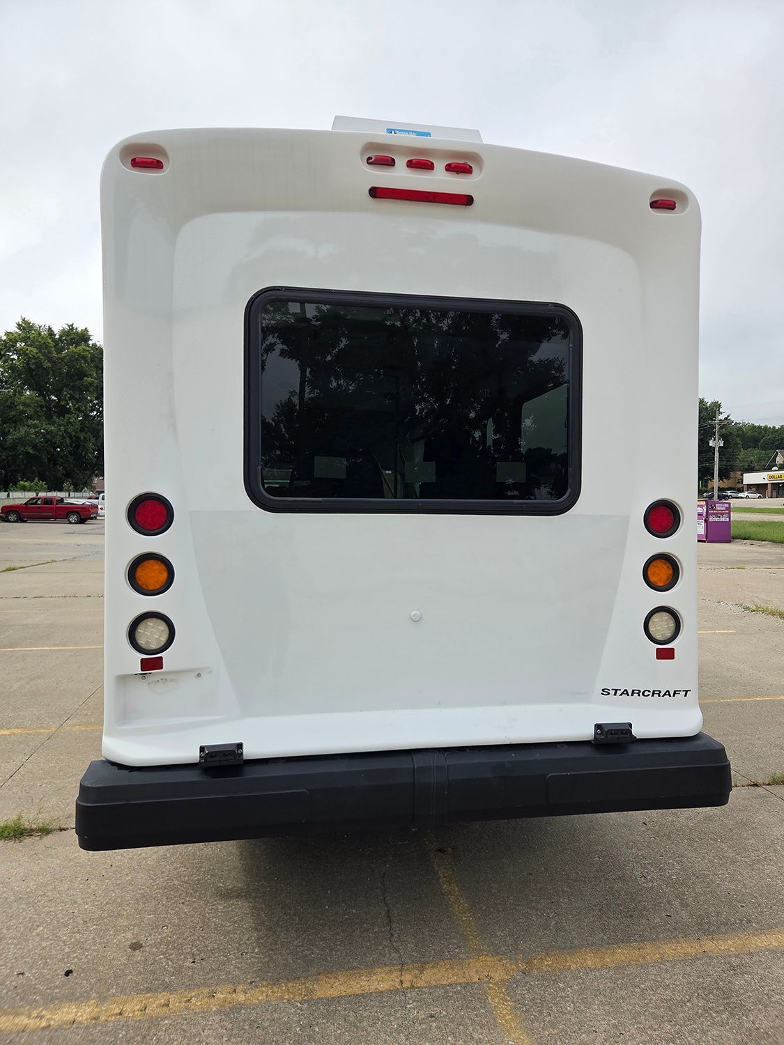 Rear view of a white shuttle bus with dark window and taillights in a parking lot
