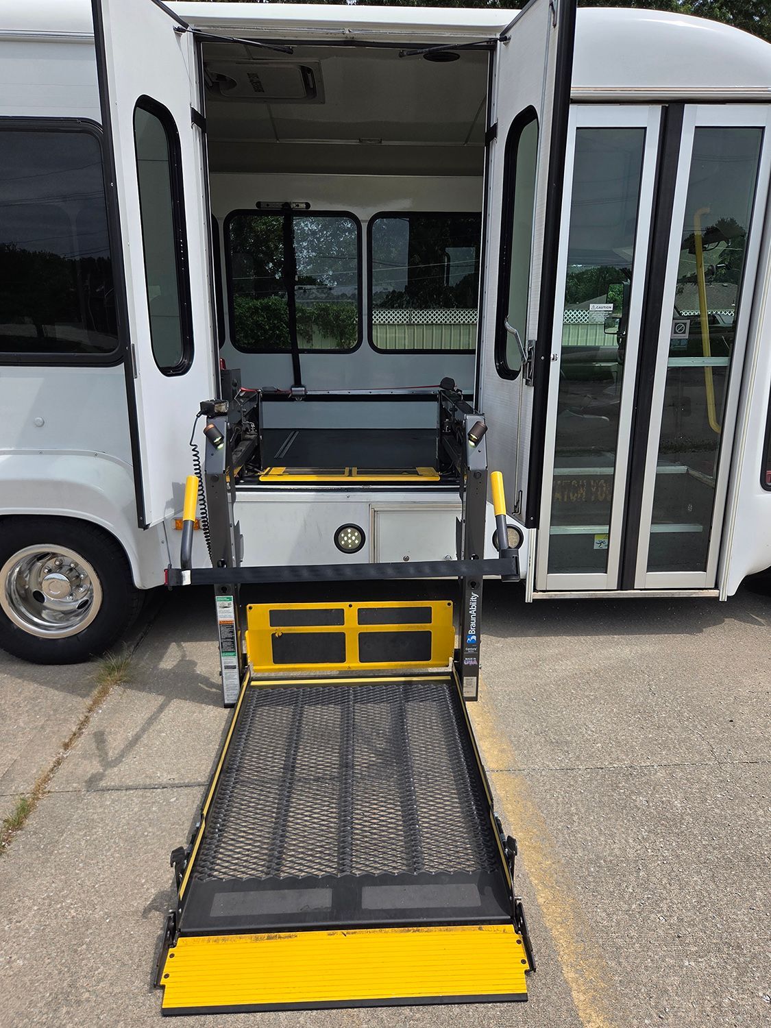 Wheelchair lift extended from a shuttle bus, with yellow safety edges and black ramp.