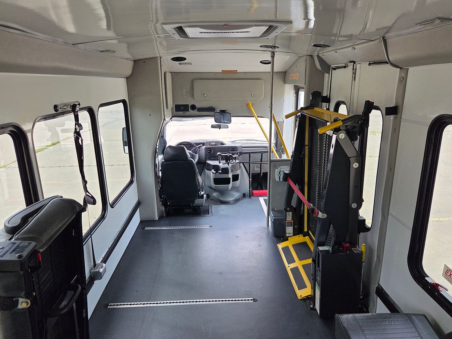 Interior of an empty bus with wheelchair lift and passenger seats, seen from the rear toward the driver area