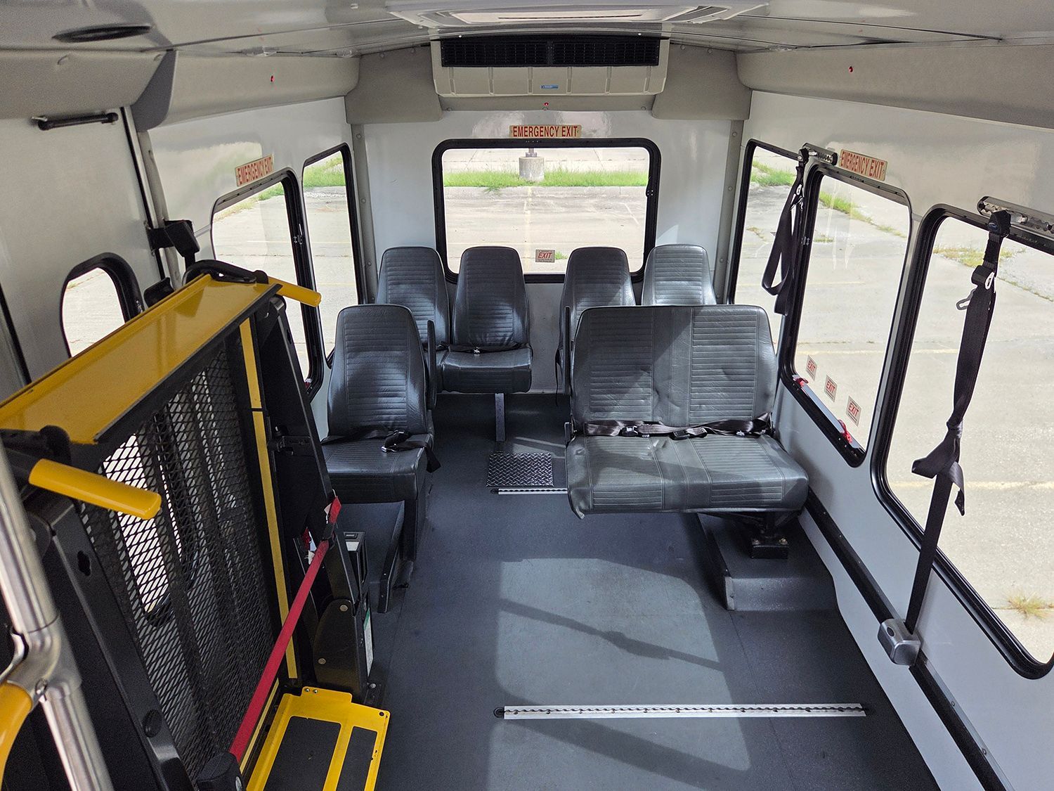 Interior of a small shuttle bus with black seats, open windows, and wheelchair-access equipment.