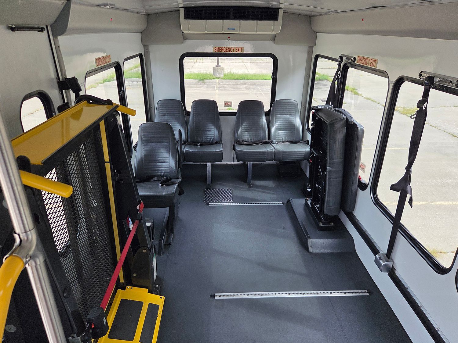 Empty bus interior with gray seats, wheelchair ramp, and open side doors.