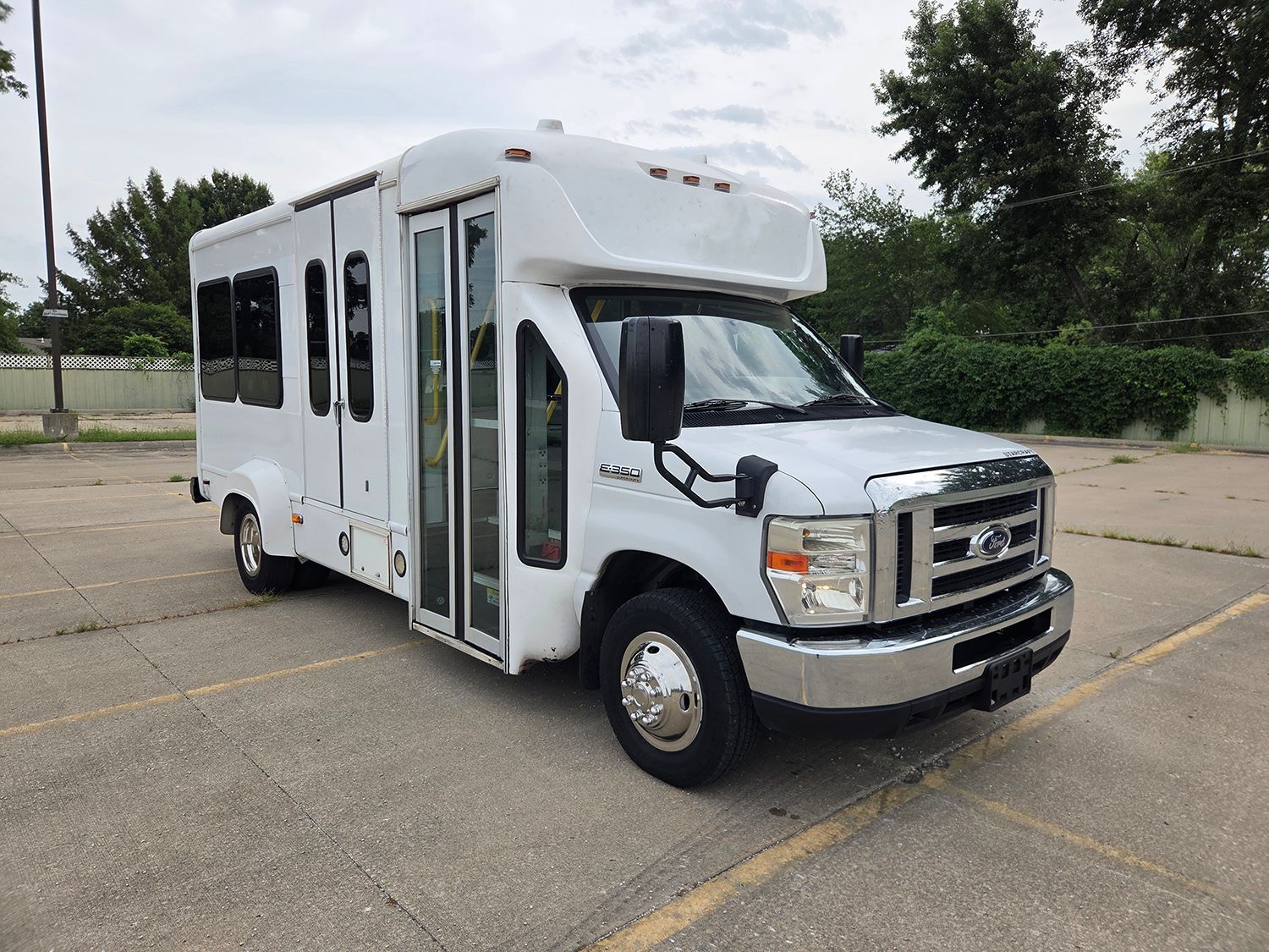 White shuttle bus parked on a concrete lot under a cloudy sky