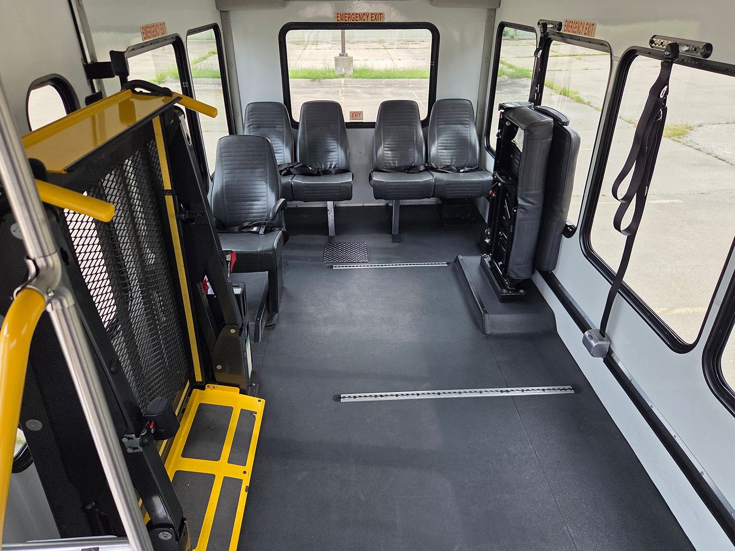Empty shuttle bus interior with black seats, yellow handrails, and large windows