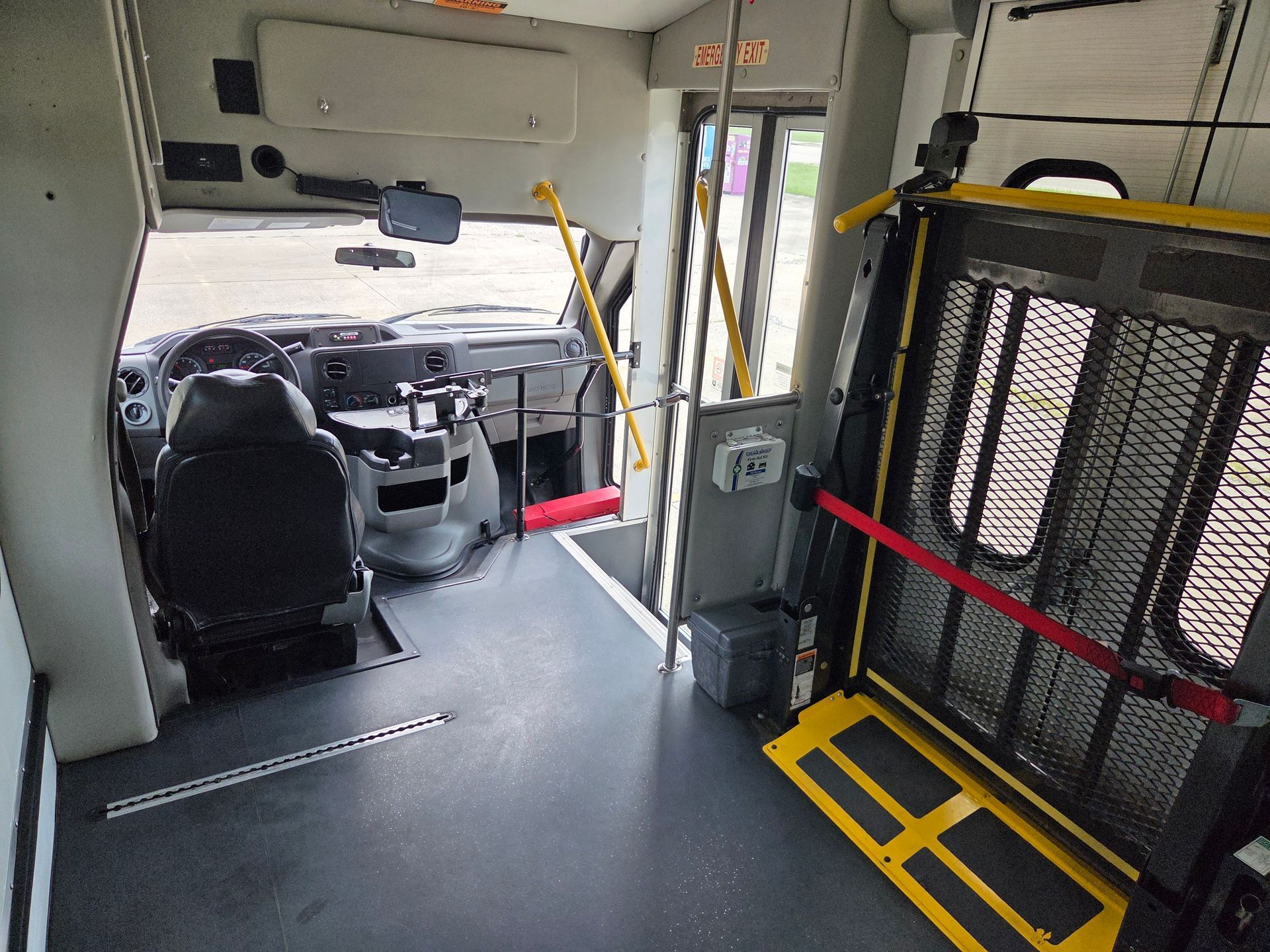 Inside a bus front cabin with driver seat, steering wheel, and yellow handrails near the wheelchair area.